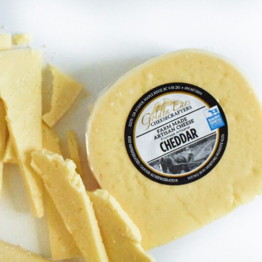 A block of cheddar cheese with a label and broken cheese pieces.